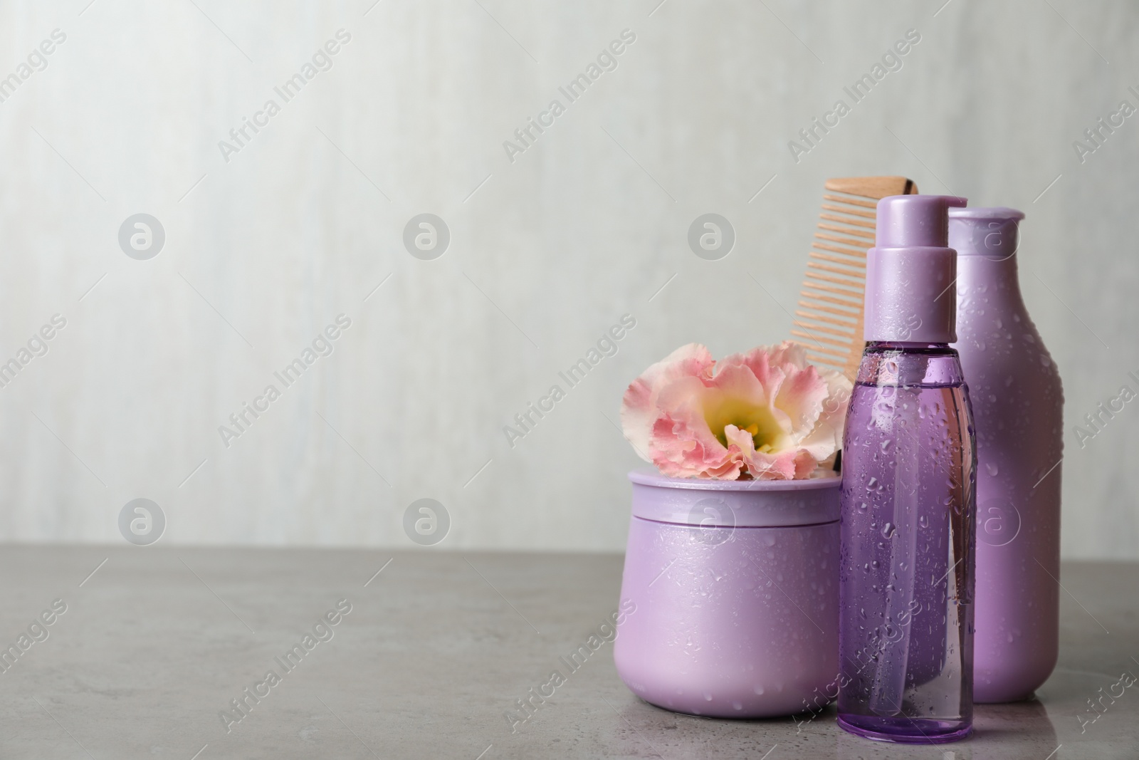 Photo of Different hair products, flower and wooden comb on grey table. Space for text