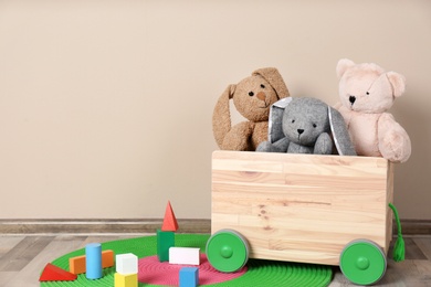 Wooden cart with stuffed toys and constructor on floor against light wall. Space for text