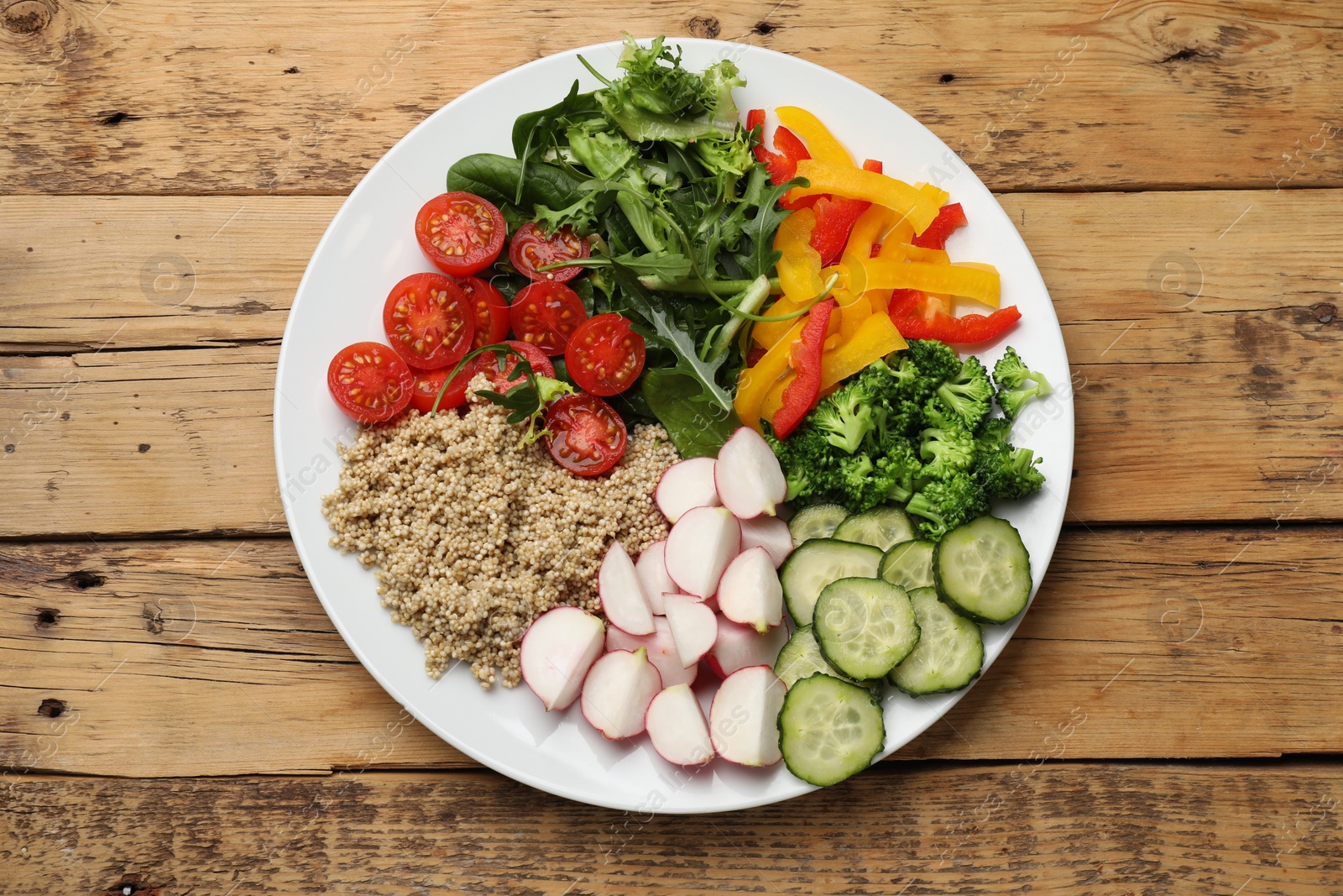 Photo of Vegetarian diet. Plate with tasty vegetables and quinoa on wooden table, top view