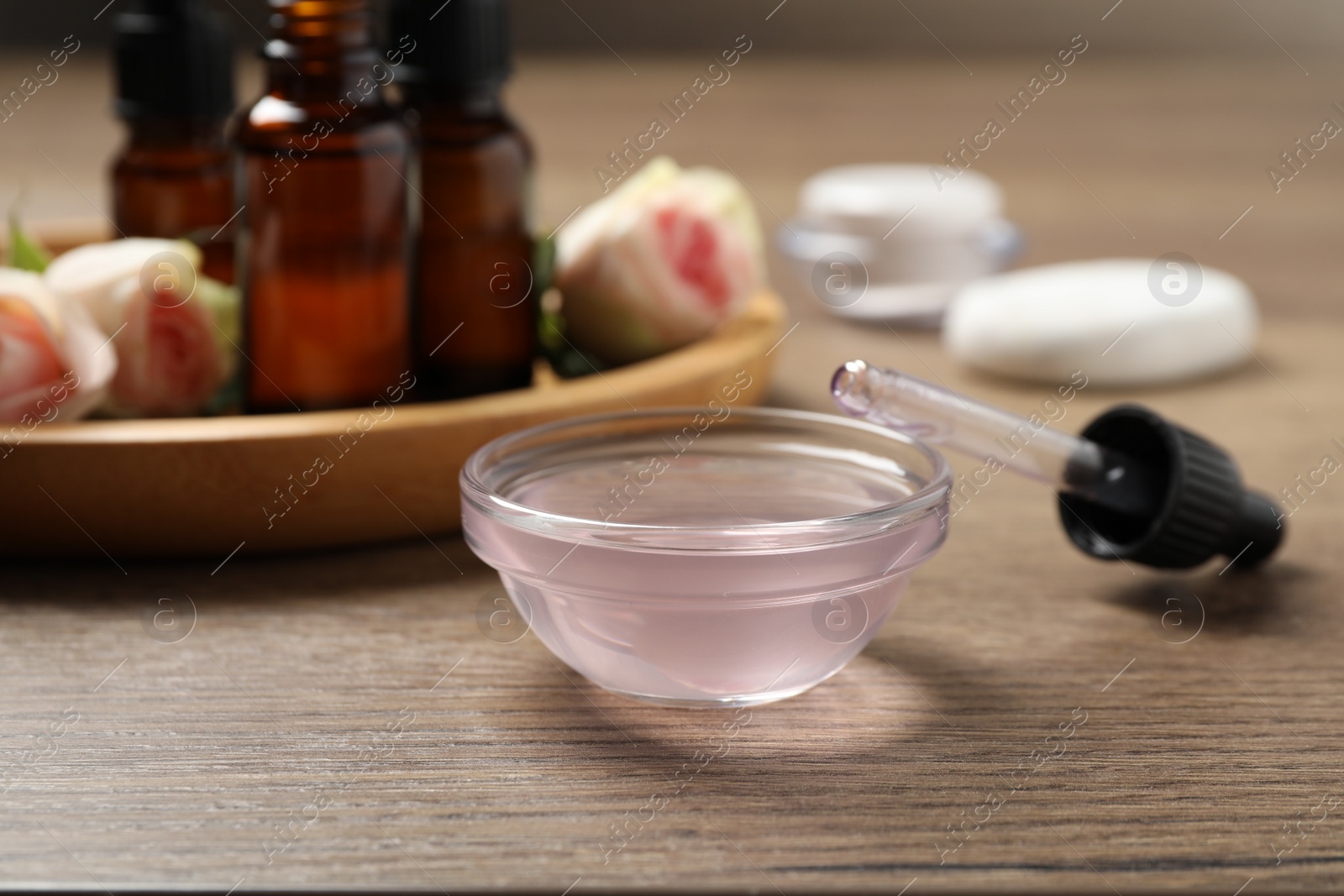 Photo of Rose essential oil in bowl and pipette on wooden table, closeup