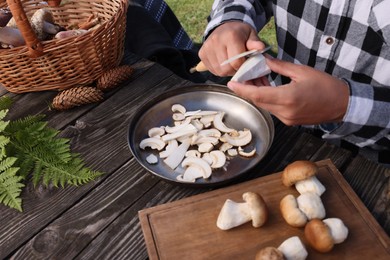Photo of Man slicing mushrooms at wooden table outdoors, closeup