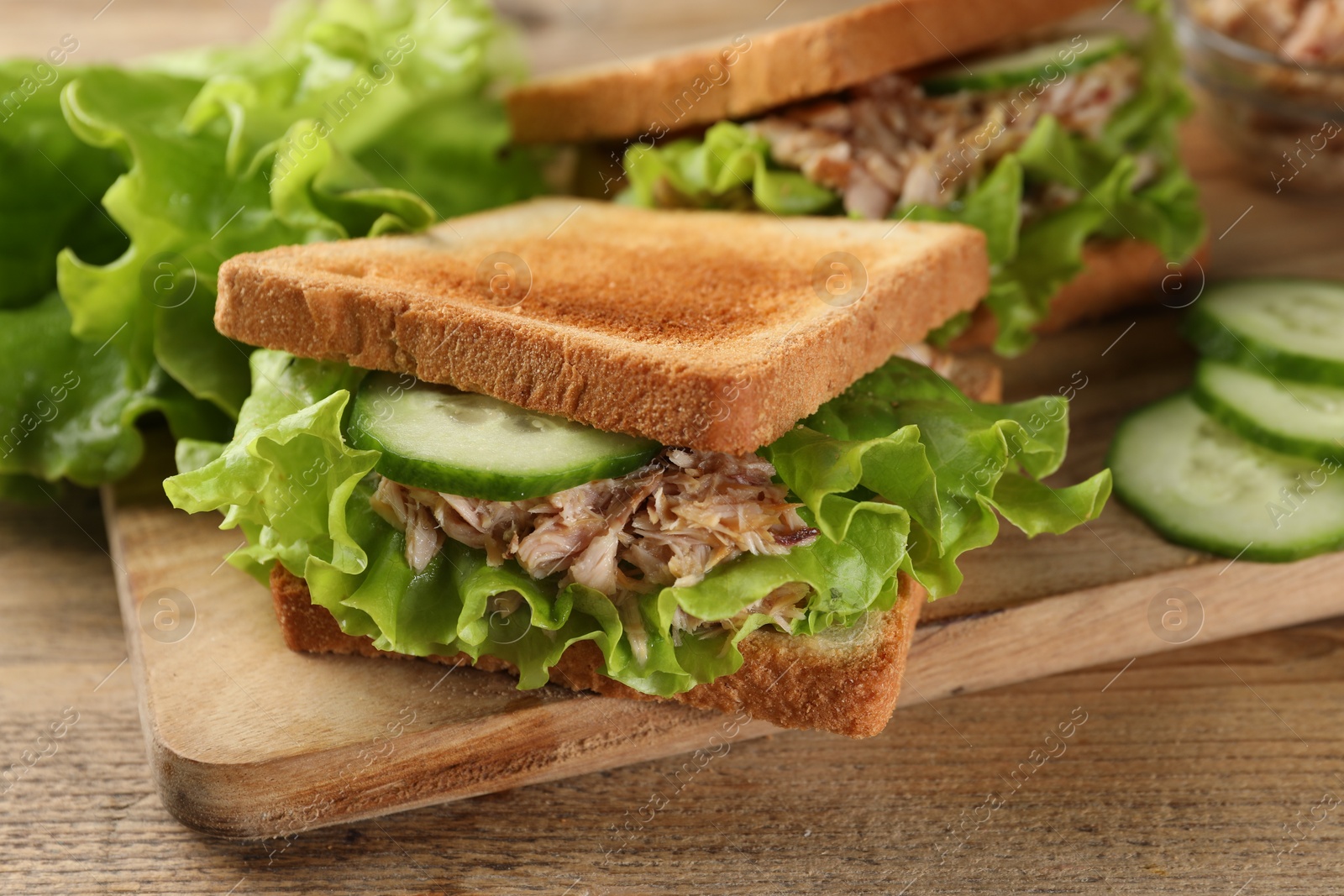 Photo of Delicious sandwiches with tuna, cucumber and lettuce leaves on wooden table, closeup