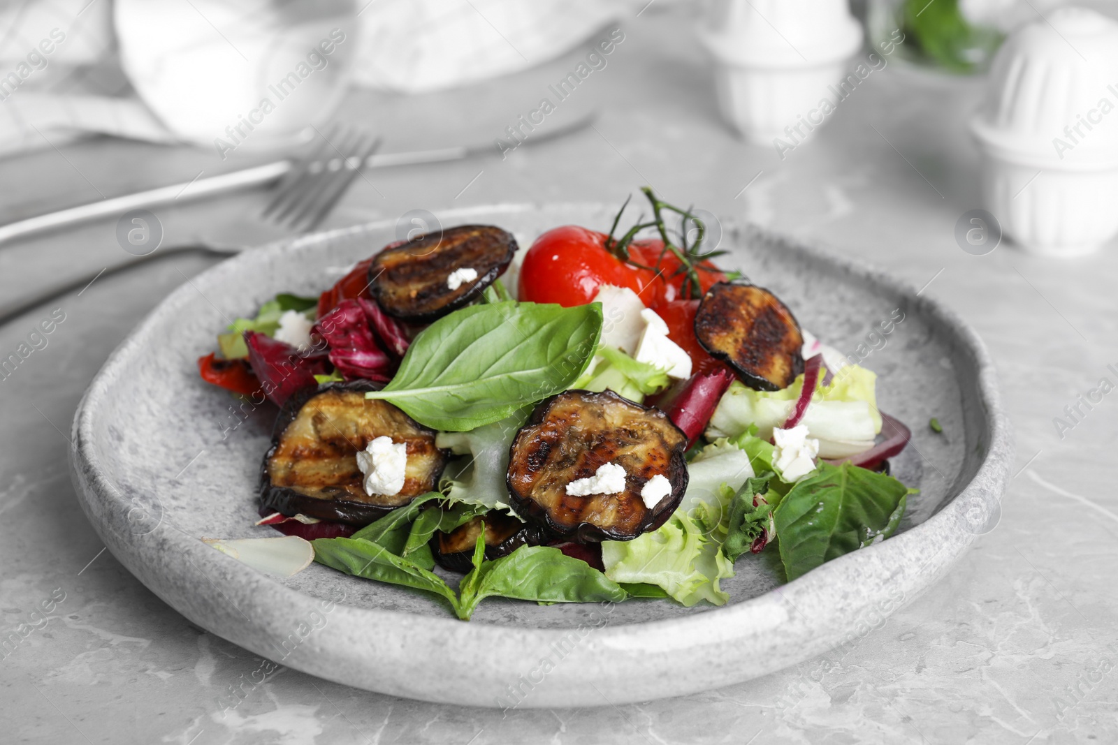 Photo of Delicious salad with roasted eggplant, basil and cheese served on grey marble table