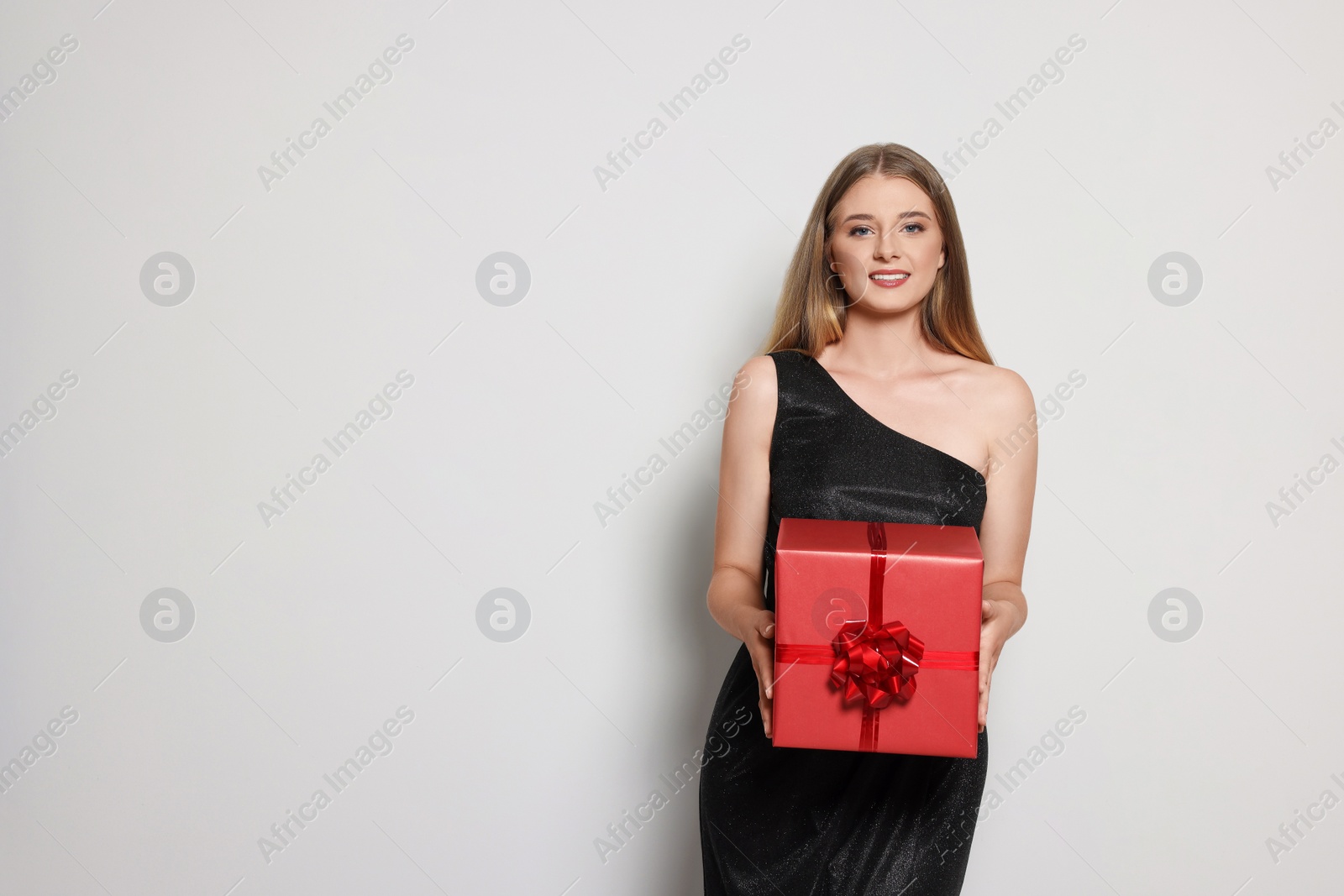 Photo of Portrait of beautiful young woman in elegant black dress with red gift box on white background, space for text