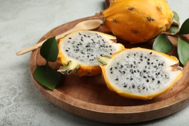 Photo of Wooden plate with delicious cut and whole dragon fruits (pitahaya) on table, closeup