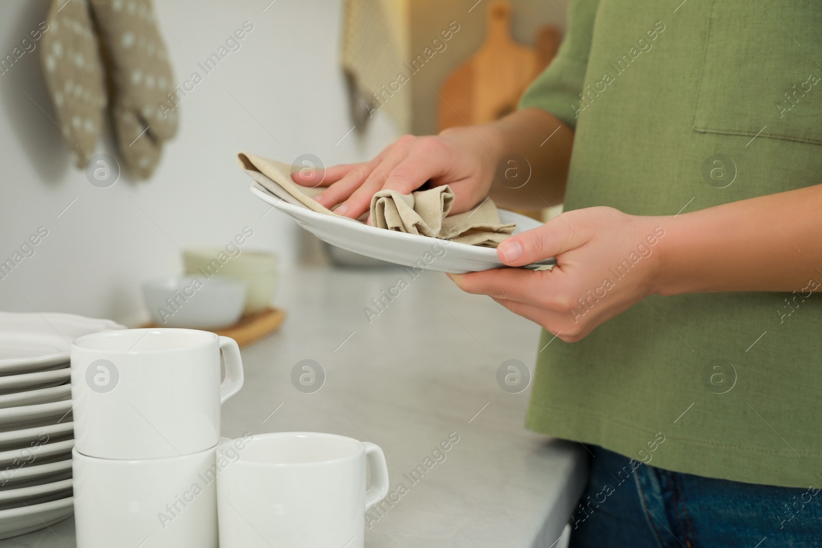 Photo of Woman wiping plate with towel at white table in kitchen, closeup