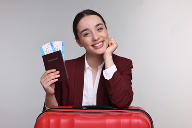 Happy businesswoman with passport, tickets and suitcase on grey background