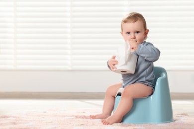 Photo of Little child with toilet paper roll sitting on plastic baby potty indoors. Space for text
