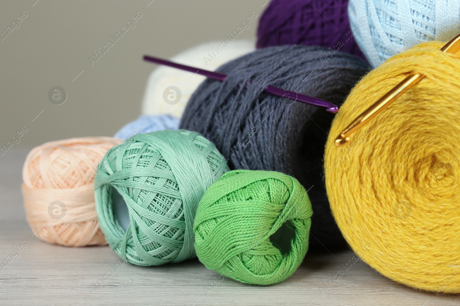 Photo of Clews of colorful knitting threads and crochet hooks on white wooden table, closeup