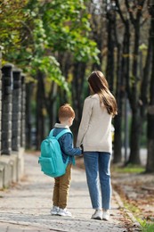 Photo of Young mom taking her son to school, back view