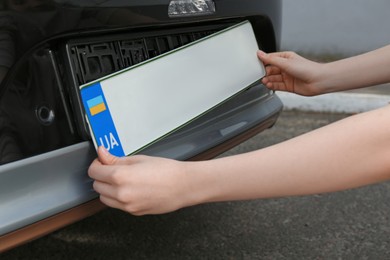 Photo of Woman installing vehicle registration plate outdoors, closeup