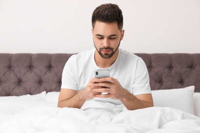 Young man addicted to smartphone in bed at home