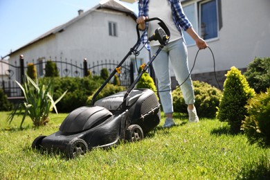 Photo of Woman cutting green grass with lawn mower in garden, closeup