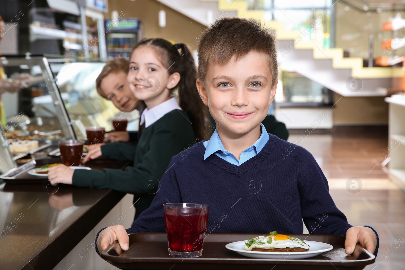 Photo of Cute boy holding tray with healthy food in school canteen