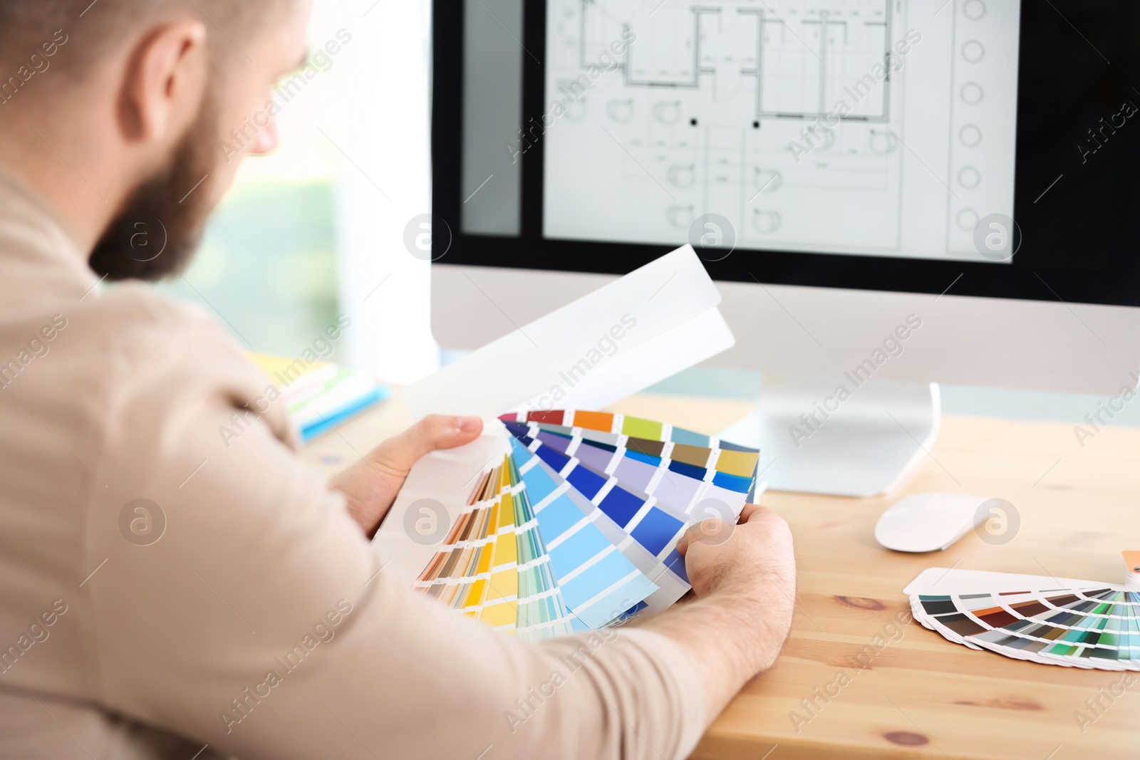 Photo of Designer with paint color palette samples at table, closeup