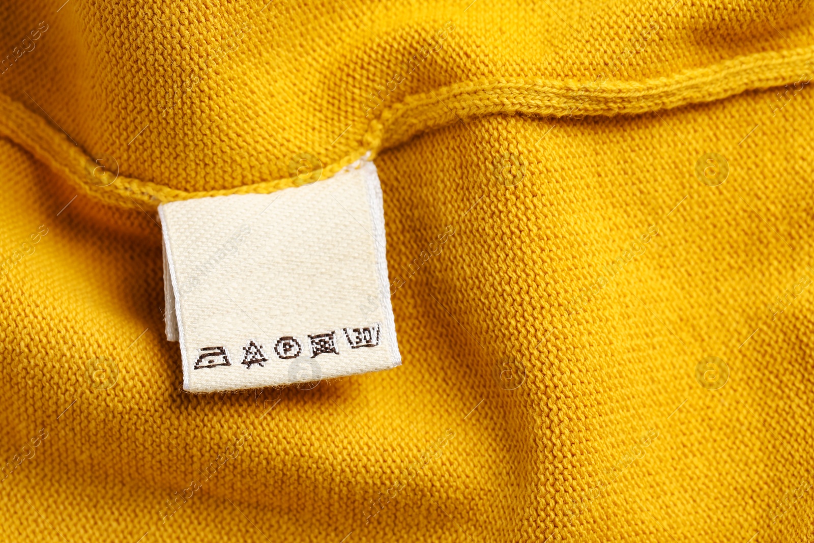 Photo of Clothing label on beautiful yellow garment, top view. Space for text