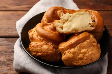Photo of Plate with delicious profiteroles with cream filling on wooden table, closeup