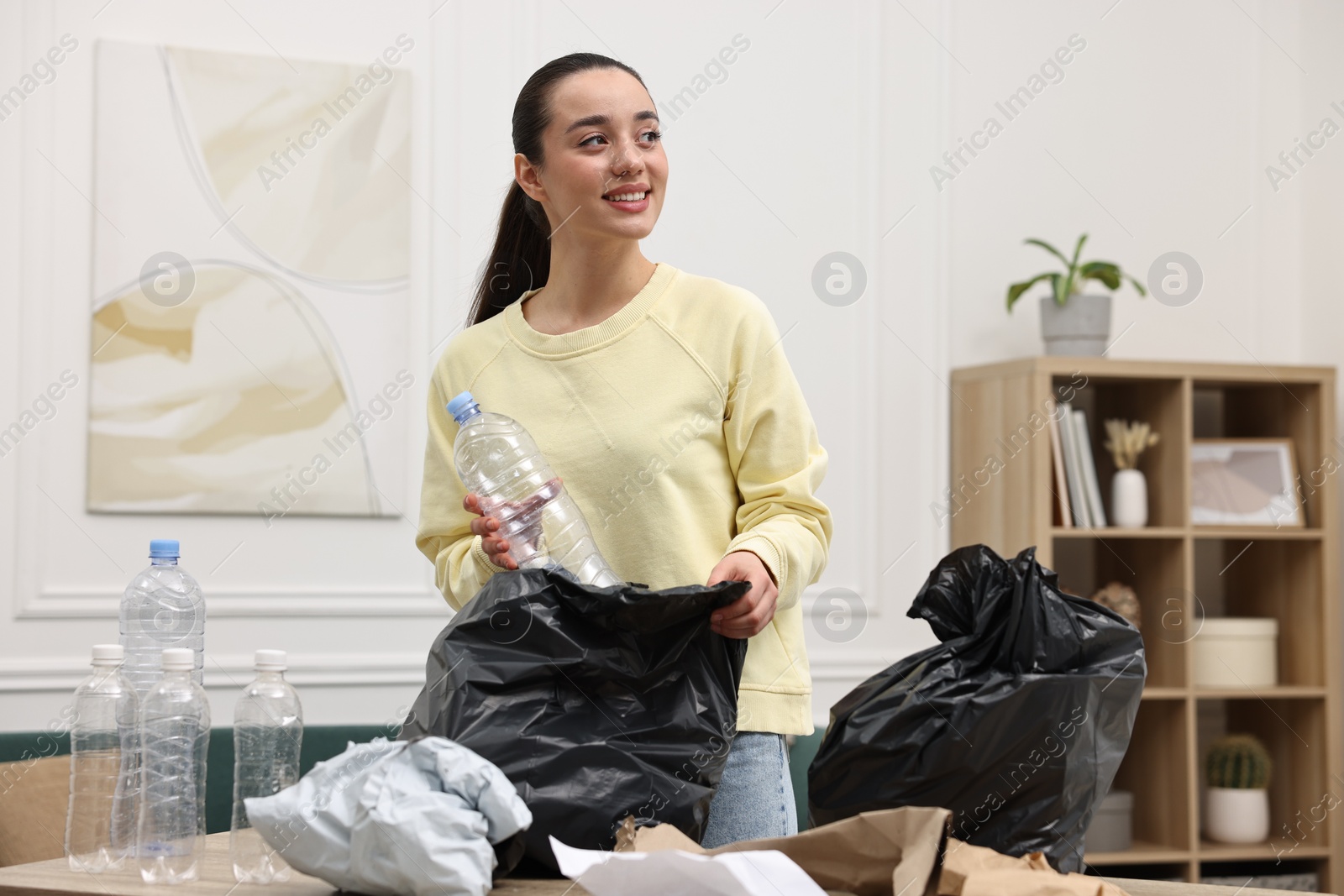 Photo of Smiling woman with plastic bag separating garbage in room