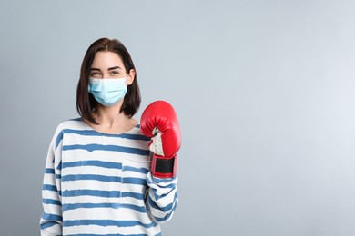 Woman with protective mask and boxing gloves on light grey background, space for text. Strong immunity concept