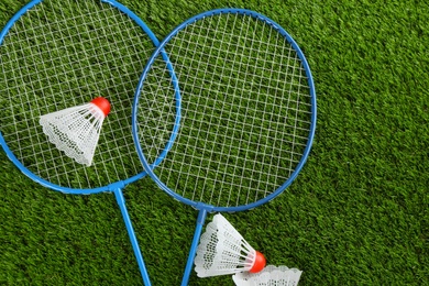 Photo of Badminton rackets and shuttlecocks on green grass outdoors, flat lay. Space for text
