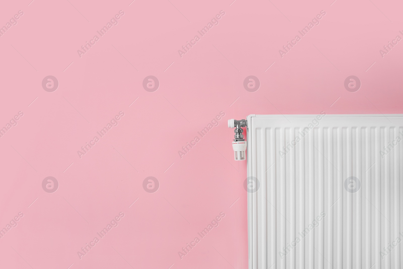 Photo of Heating radiator with thermostat near color wall. Space for text