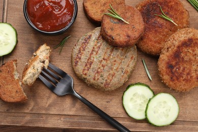 Photo of Fork with piece of delicious cutlet near tasty vegan meat products and sauce on wooden table, flat lay