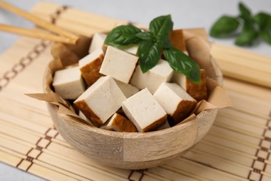 Photo of Bowl of smoked tofu cubes and basil on bamboo mat, closeup