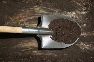 Photo of Metal shovel with fertile soil on dirty wooden surface, top view