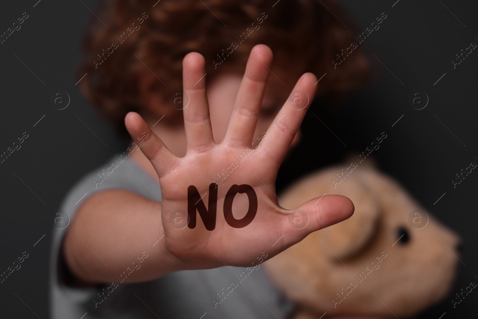 Image of Child abuse. Boy with toy making stop gesture near grey wall, selective focus. No written on his hand