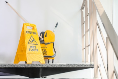 Safety sign with phrase Caution wet floor and mop bucket on stairs. Cleaning service