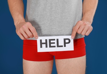 Man holding paper with word HELP on blue background, closeup. Urology problems