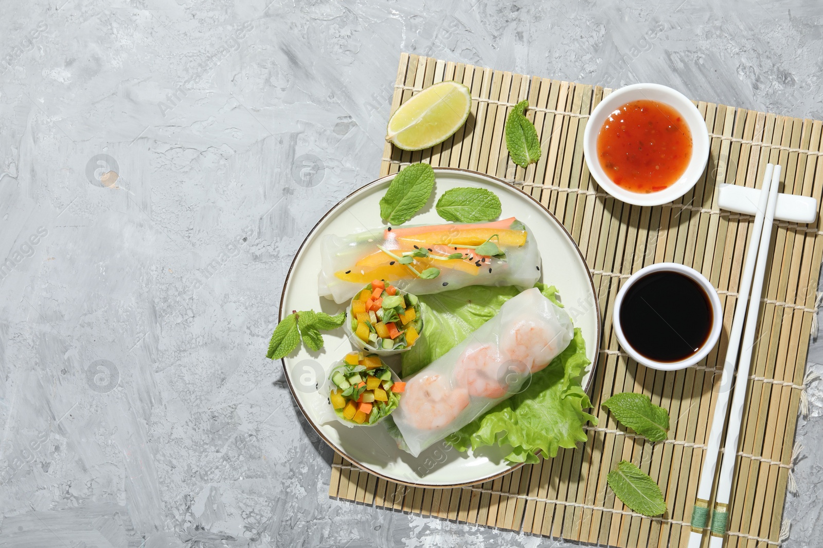 Photo of Tasty spring rolls served with sauces on grey textured table, top view. Space for text