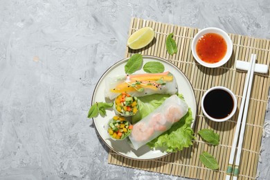 Tasty spring rolls served with sauces on grey textured table, top view. Space for text