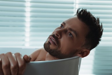 Photo of Upset man thinking about something in bathtub at home. Loneliness concept