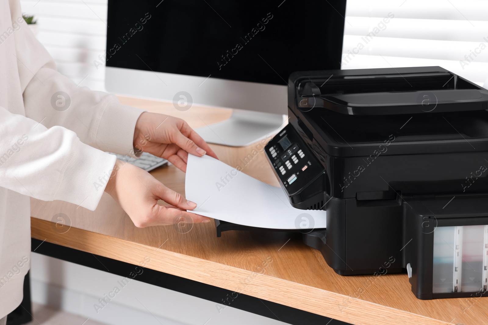 Photo of Woman loading paper into printer at wooden table indoors, closeup