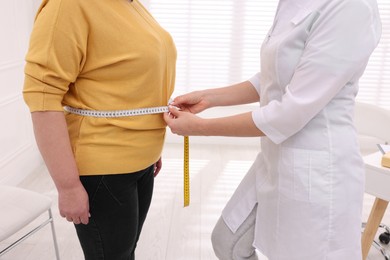 Photo of Nutritionist measuring overweight woman's waist with tape in clinic, closeup