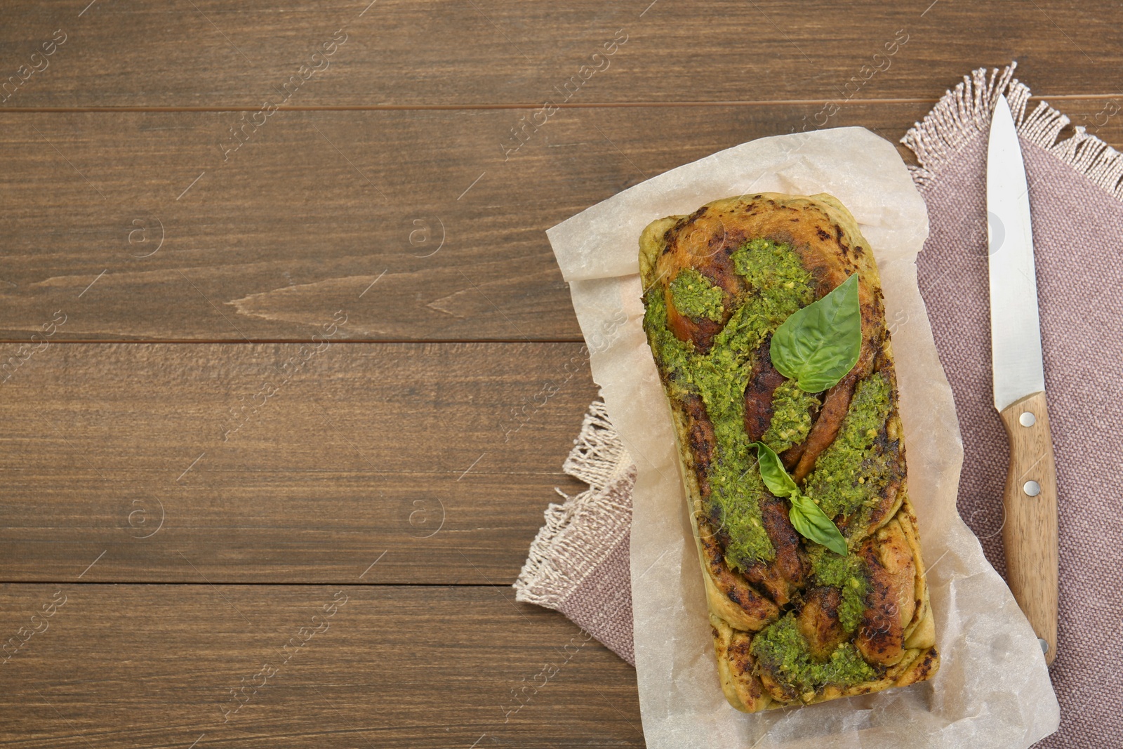 Photo of Freshly baked pesto bread with basil and knife on wooden table, flat lay. Space for text