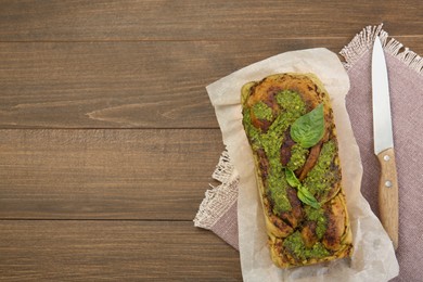 Freshly baked pesto bread with basil and knife on wooden table, flat lay. Space for text