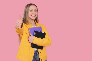 Photo of Teenage girl with notebooks showing thumb up on pink background. Space for text