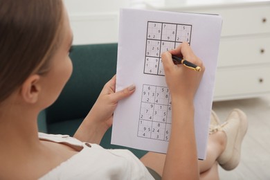 Young woman solving sudoku puzzle on sofa indoors, closeup