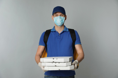 Photo of Courier in protective mask and gloves holding pizza boxes on light grey background. Food delivery service during coronavirus quarantine