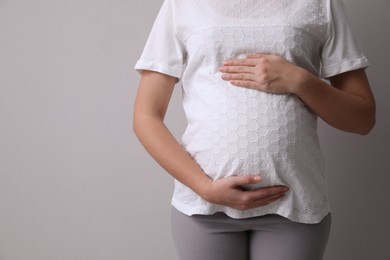 Photo of Pregnant woman on light grey background, closeup. Space for text