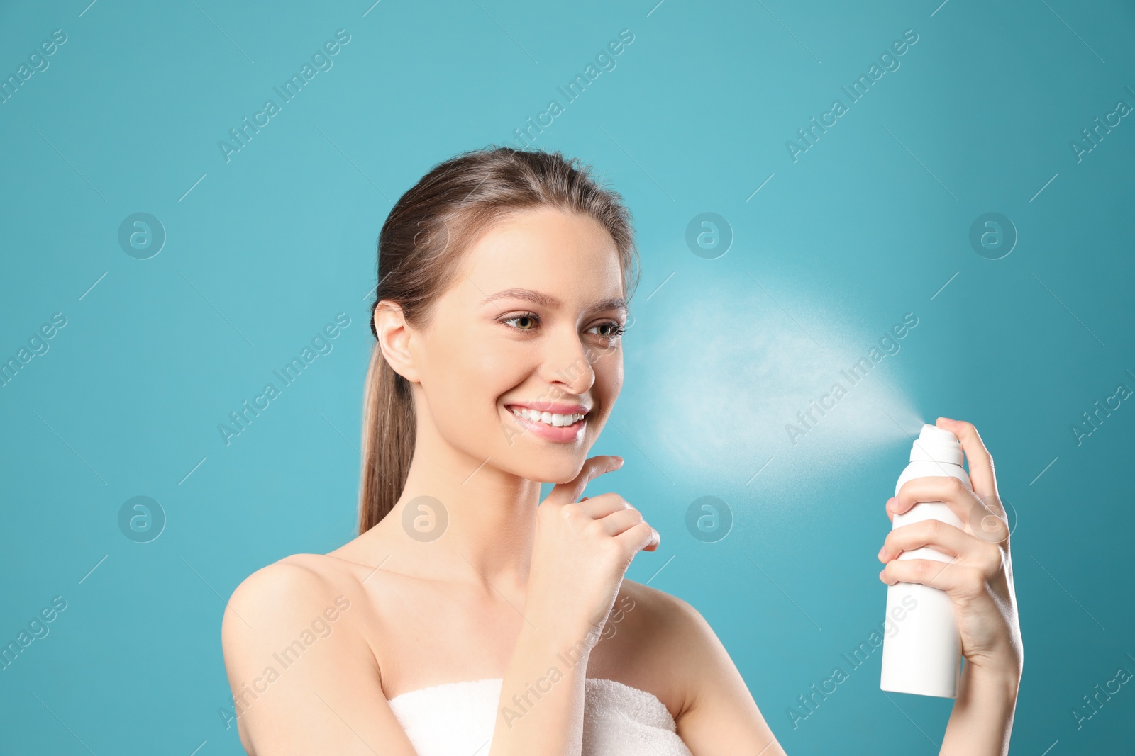 Photo of Young woman applying thermal water on face against color background. Cosmetic product