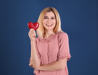 Portrait of beautiful woman holding decorative heart on color background