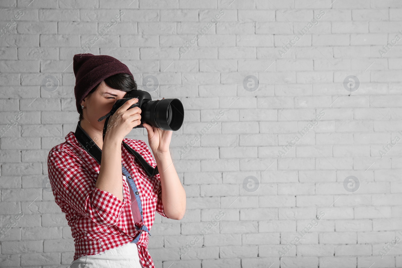 Photo of Young female photographer with camera on brick background