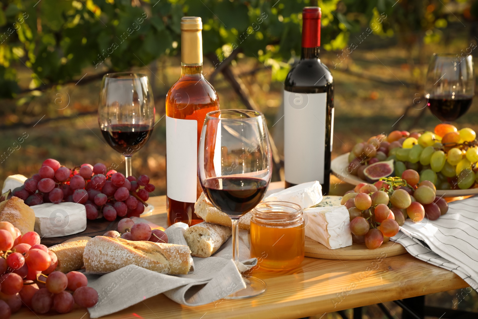 Photo of Red wine and snacks served for picnic on wooden table outdoors