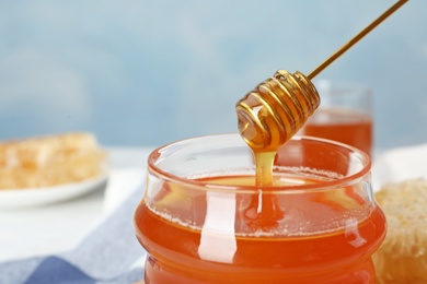 Sweet honey dripping from dipper into glass jar, closeup