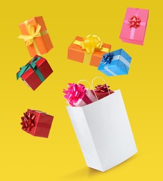 Image of Many different gift boxes falling into paper shopping bag on yellow background