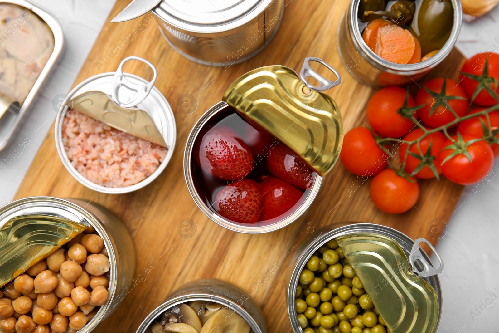 Photo of Open tin cans with different preserved products on wooden board, flat lay