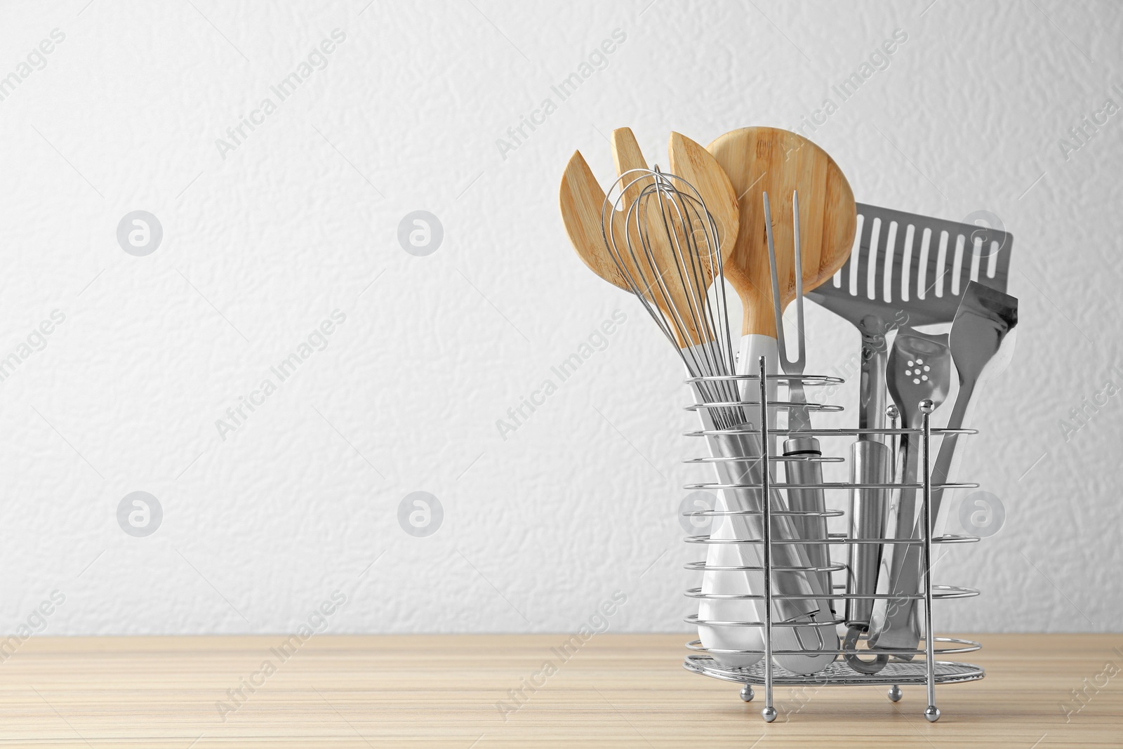 Photo of Set of kitchen utensils in stand on wooden table near light wall. Space for text